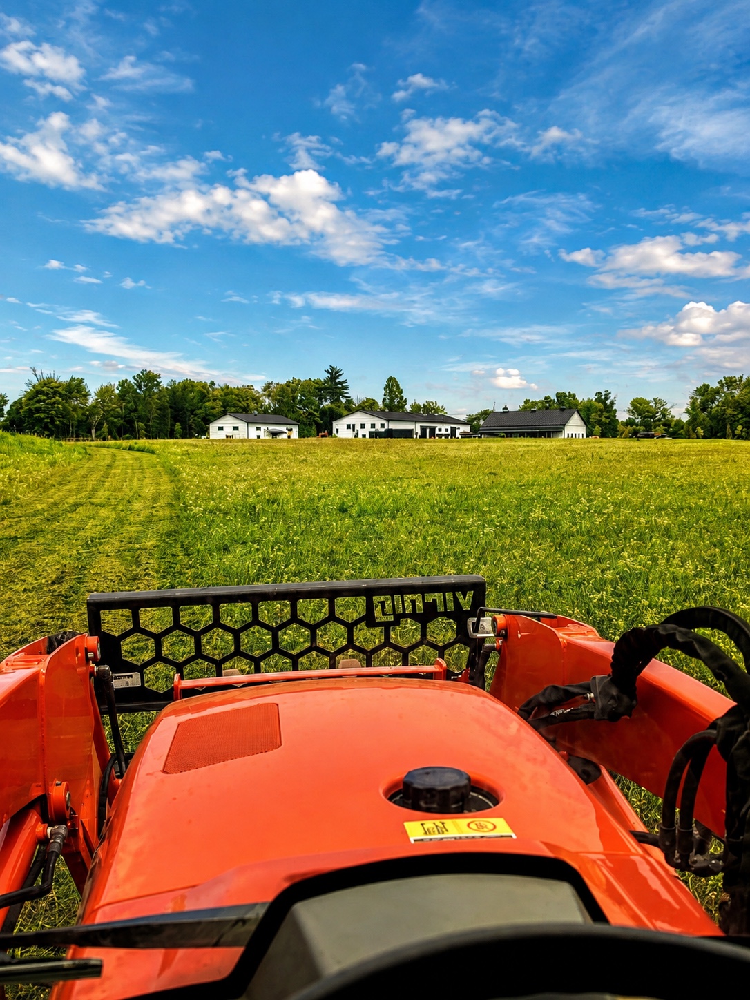 View from the tractor across a freshly mowed field toward the barns at Baldwins Creek Farm