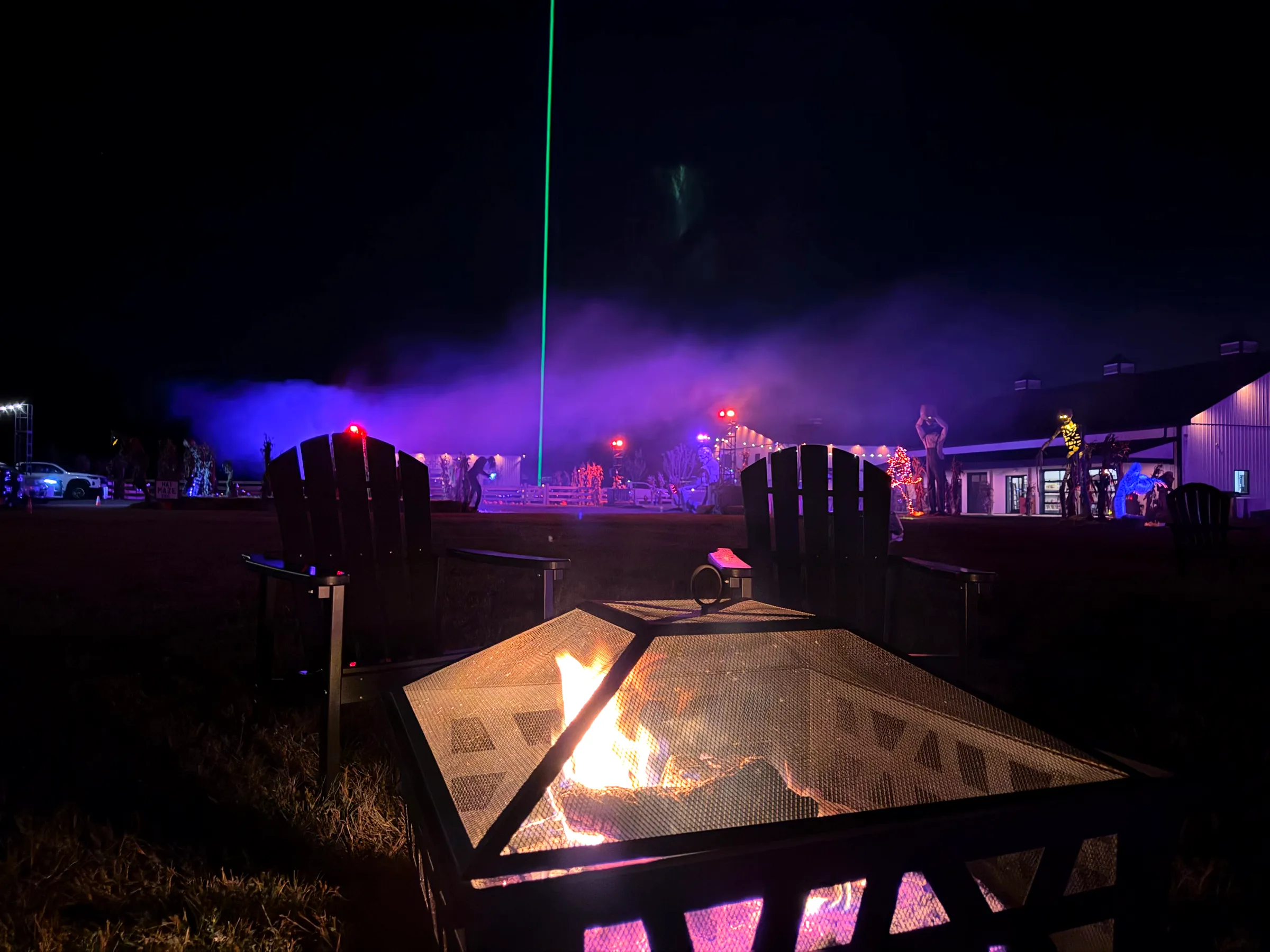 Baldwins Creek Farm - Hopewell Township, NJ: fire pit and Adirondack chairs at night with purple fog, a green laser and lit Halloween animatronics by the market